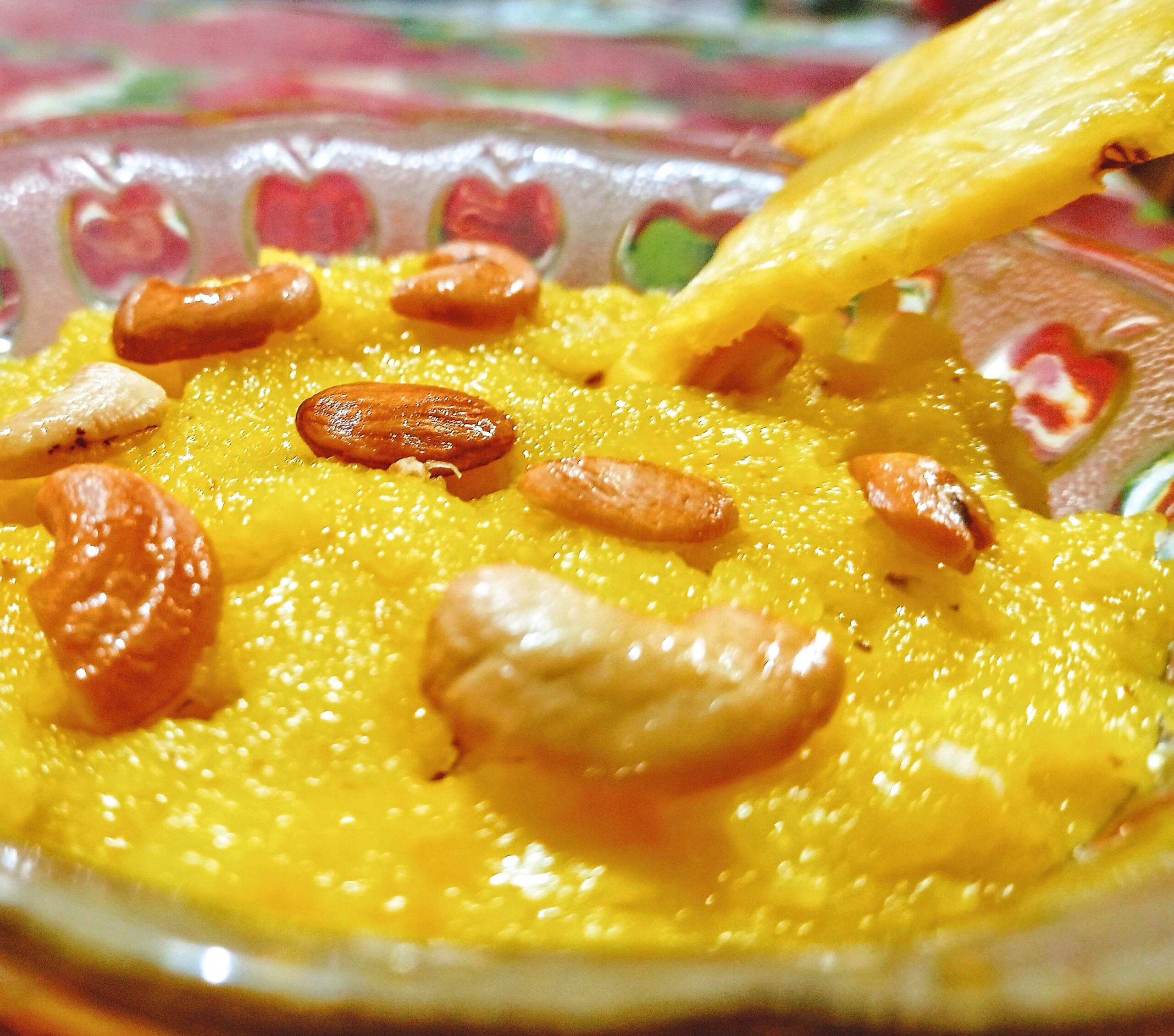 Pineapple Kesari Preparation time: 40 minutes.  Serves: 6  Ingredients 1/2 cup ghee of good quality 1/2 cup peanut oil 1/2 cup dried raisins 1/2 cup cashews 1 tsp saffron 1 cup pineapple pieces 1 cup semolina 2 tsp cardamom powder 3/4 cup sugar a pinch salt  Method Peeling the pineapple can be a bit difficult. Use a knife and slice off the thick rind and remove the “eyes.” Cut the flesh into small cubes. Soak the saffron in two tbsp hot water until it releases a nice reddish-orange color. Use a heavy-bottomed saucepan over medium heat. Mix the ghee and oil, pour into the pan and heat gently. Set aside half of this mixture in a separate bowl. Fry the cashews and raisins on low heat for one to two minutes, until the raisins swell and the cashews turn golden brown. Add the semolina and stir-fry for three to four minutes until it becomes aromatic and lightly golden. Stir in the saffron, pineapple, sugar and salt. Add 2 cups of boiling water, stirring constantly to avoid lumps. Add the reserved ghee mixture and stir well. Add the cardamom powder and mix. Cover and simmer on low heat for five minutes. Turn off the heat, stir and let rest for ten minutes before serving. Share and enjoy.
